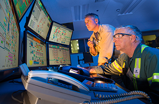 Two Cameco employees looking at data on six computer monitors